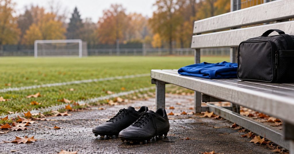 Scarpe da calcio, una maglia blu e una borsa su una panchina generica a bordo campo. Immagine illustrativa generata con AI.