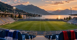 Illustrazione AI di uno stadio calcistico sul lago, senza giocatori né loghi; copertina del Como-Venezia.